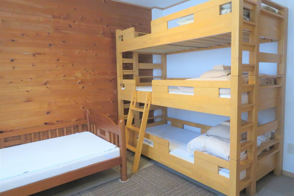 Una litera, una cama individual y una pared de madera.