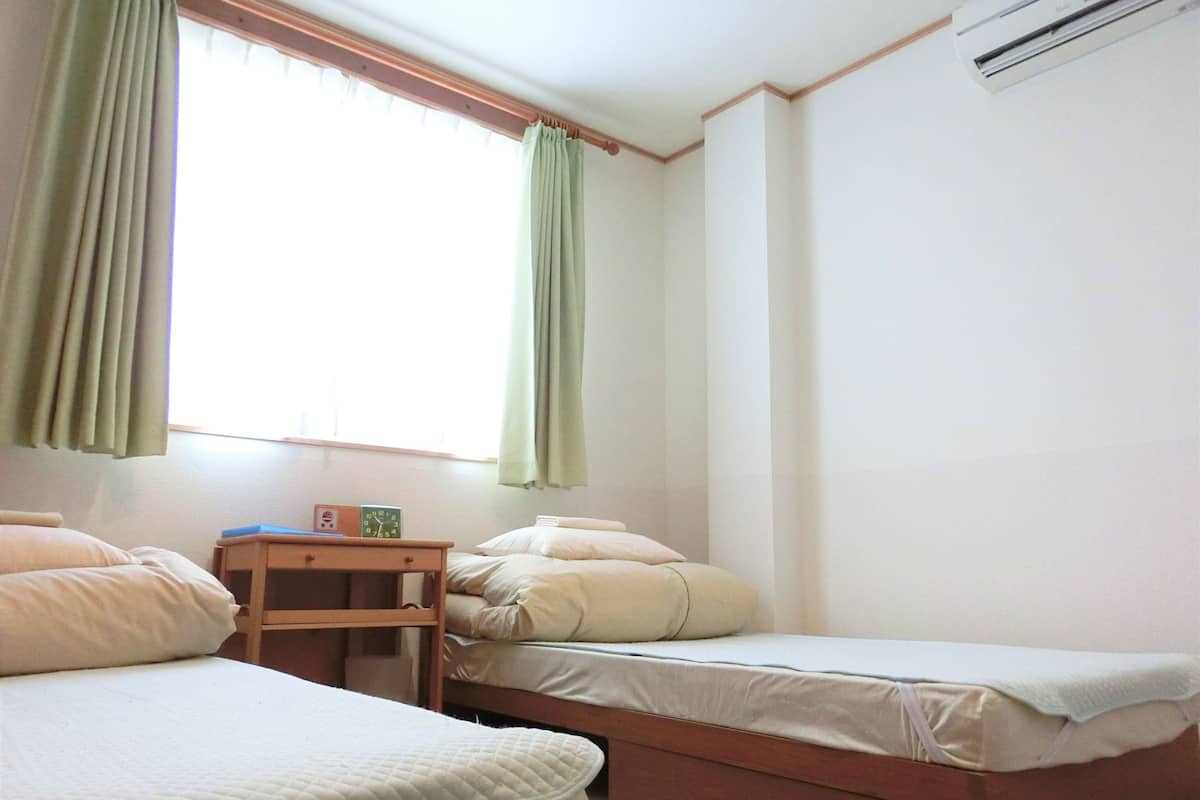 Una habitación con dos camas, una mesita de noche de madera, un reloj y una ventana con cortinas.