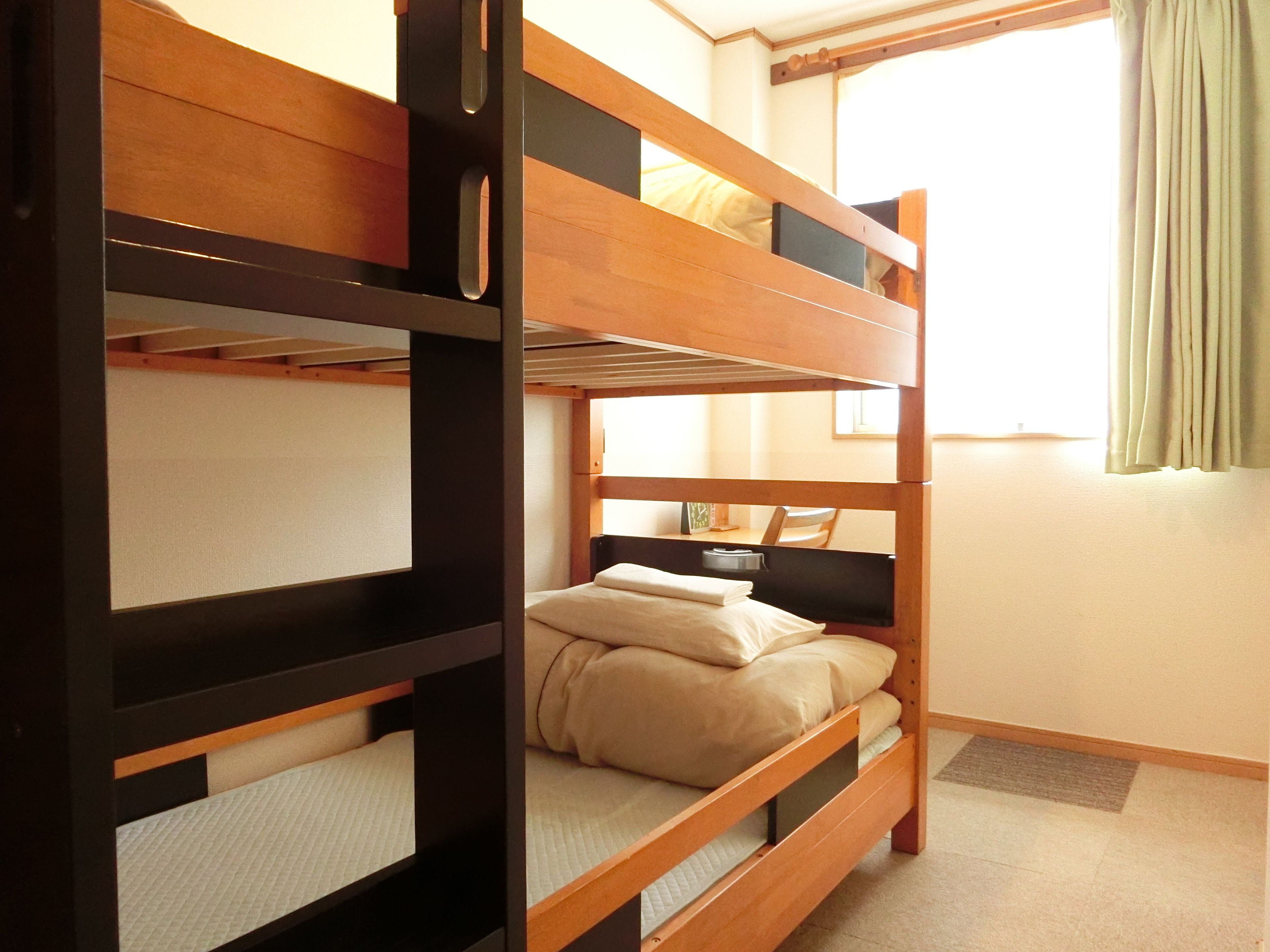 Une chambre avec un lit superposé, un bureau et une chaise, une fenêtre avec des rideaux et une porte.