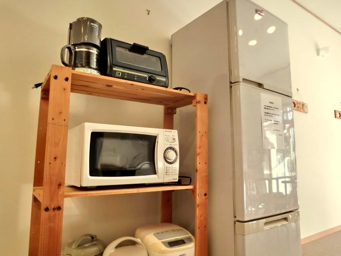 A kitchen with a microwave, toaster, and coffee maker on a wooden shelf, and a refrigerator.