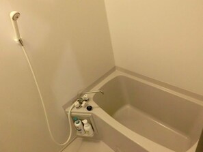 Un baño con bañera, ducha y estante con artículos de aseo.