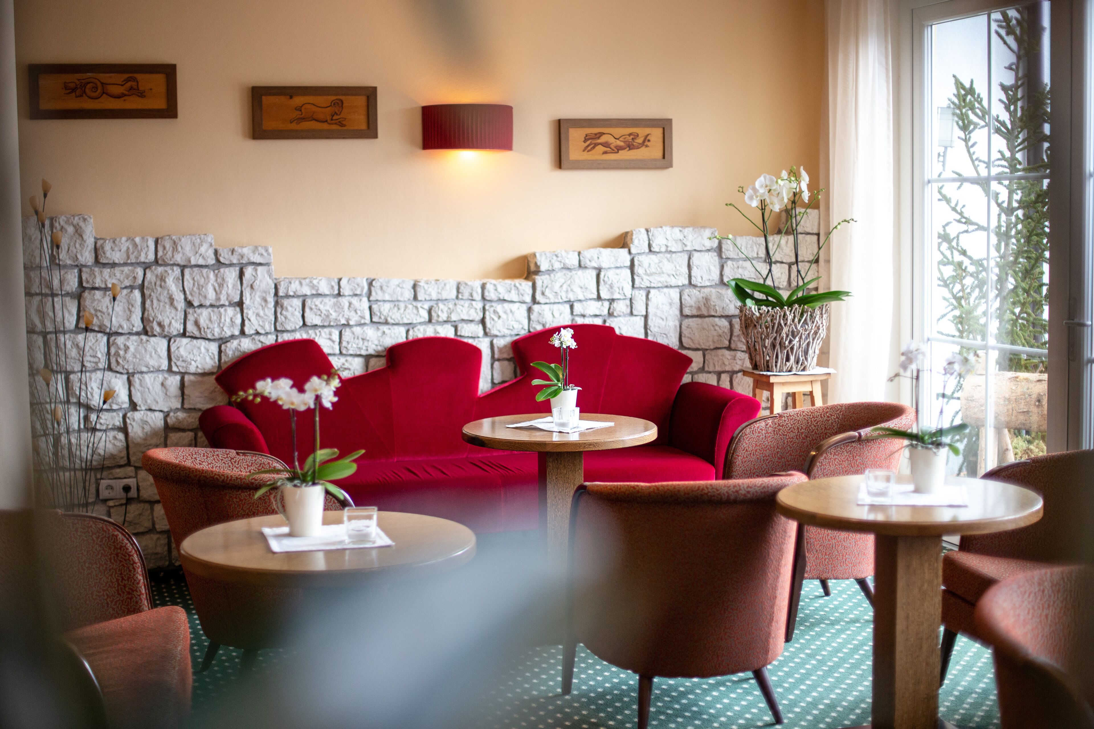 Een gezellige zithoek met een stenen muur, rode banken en ronde tafels met potplanten.