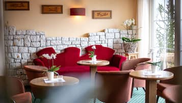 Een gezellige zithoek met een stenen muur, rode banken en ronde tafels met potplanten.