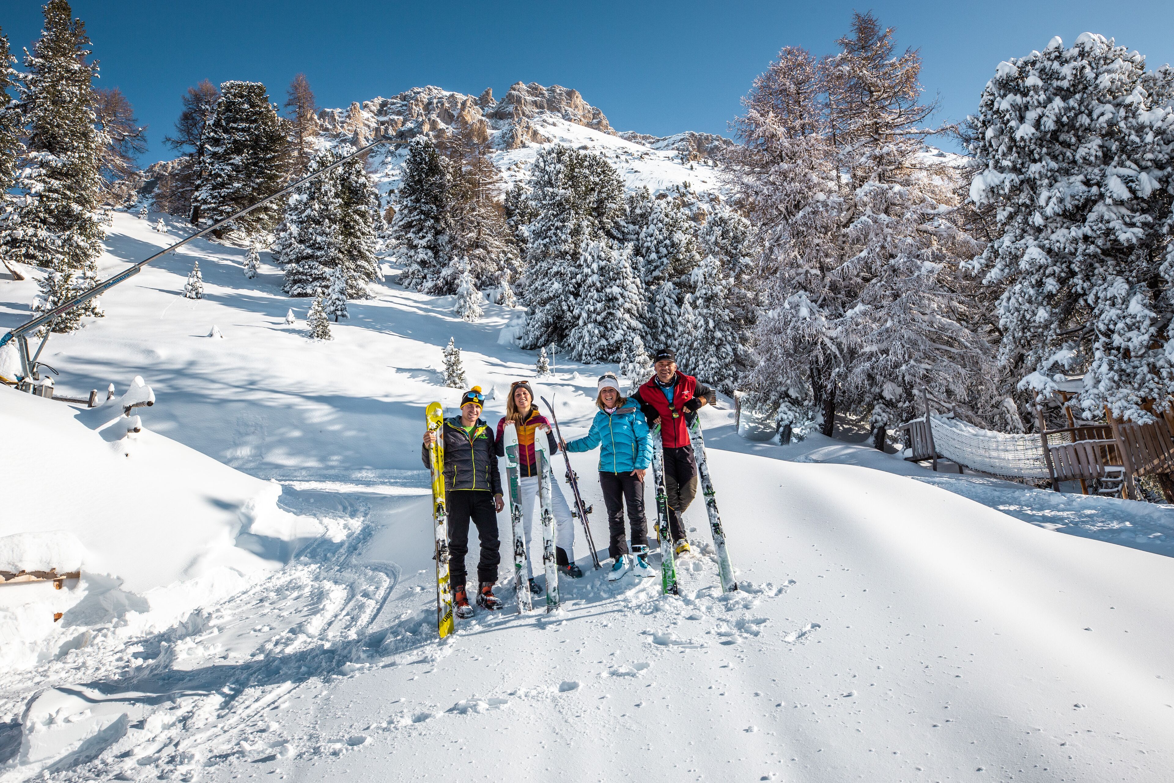 A group of people standing on a snow-covered ski slope with trees in the background.