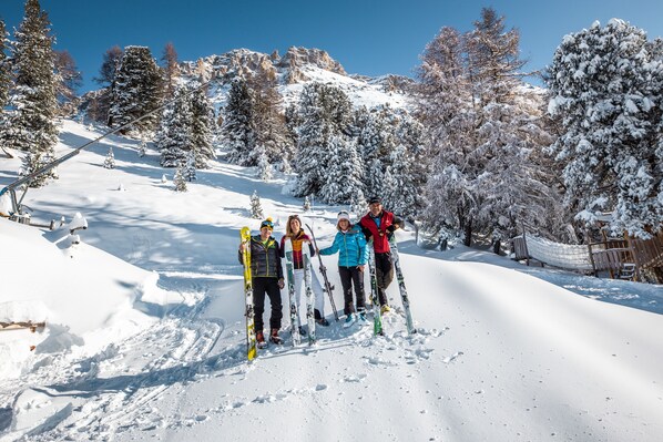Um grupo de pessoas em uma encosta nevada para esquiar, com árvores ao fundo.