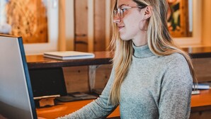 A person seated at a wooden table with a laptop, in a room with wooden walls and a hanging light fixture. - Hotel Marica (Nova Ponente)