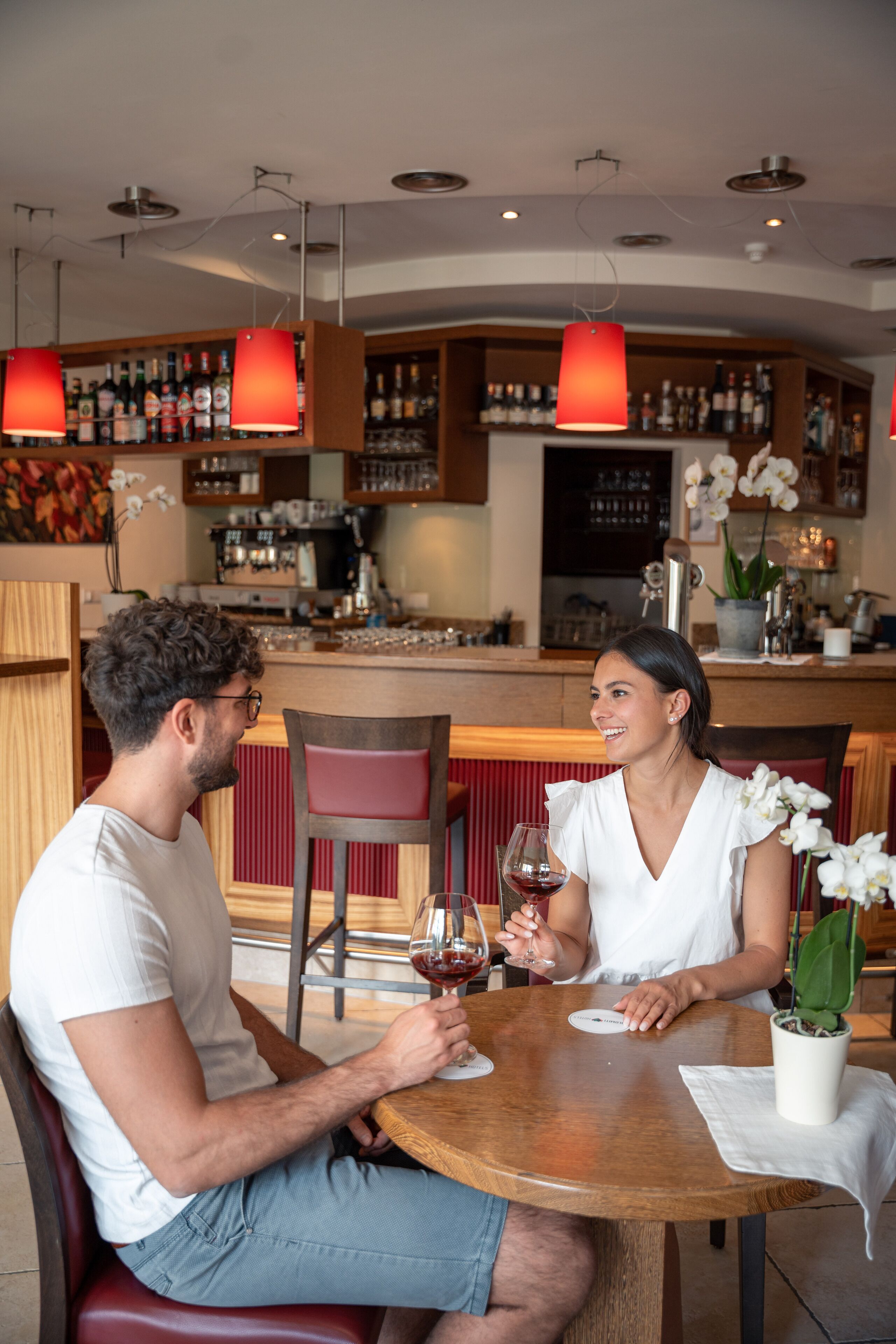 Ein Paar sitzt an einem runden Holztisch in einem Restaurant, im Hintergrund ist eine Bar zu sehen.