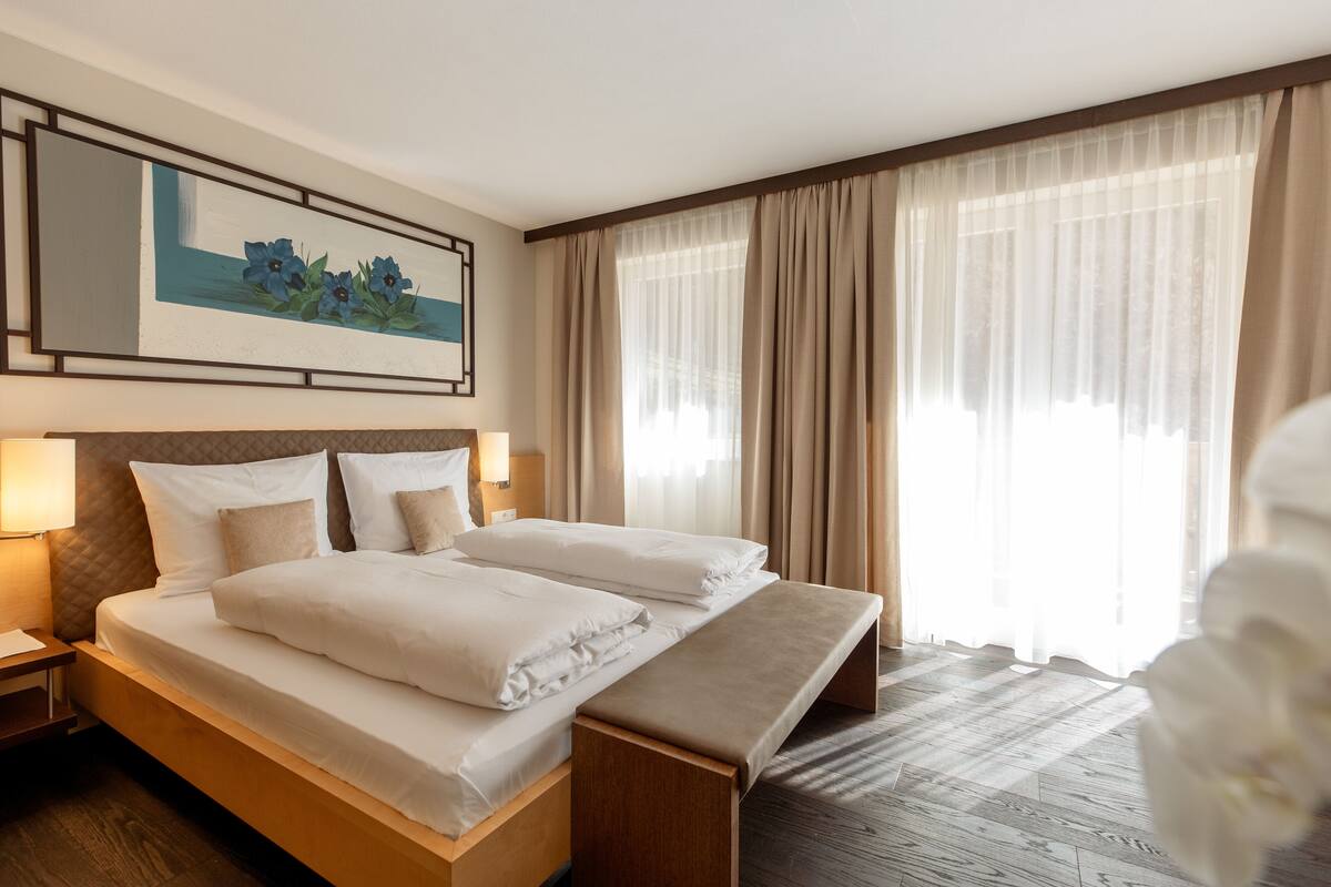 A hotel room with a large bed, bedside tables, a bench, and a painting on the wall.