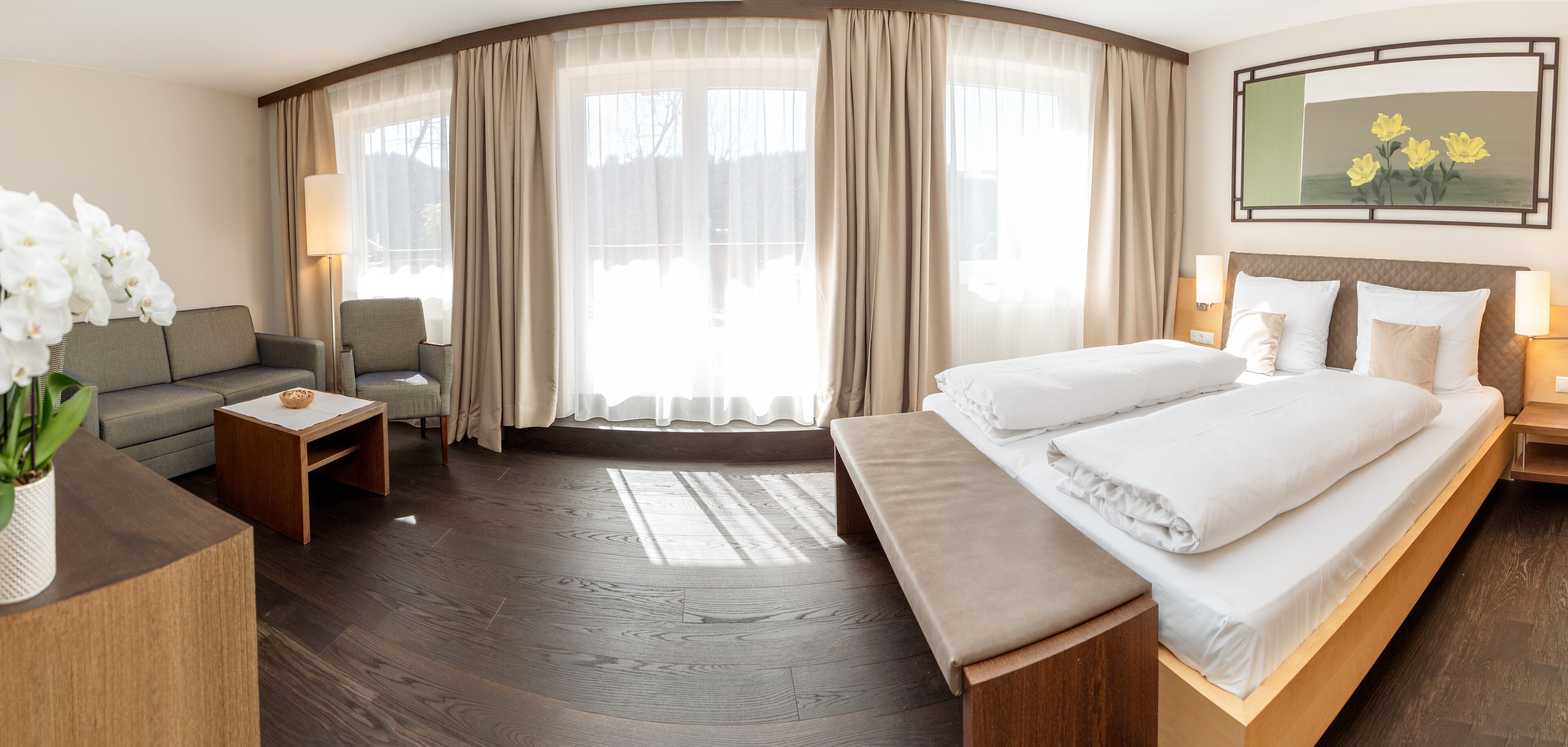 A hotel room with a large bed, a sofa, a small table, and a bench.