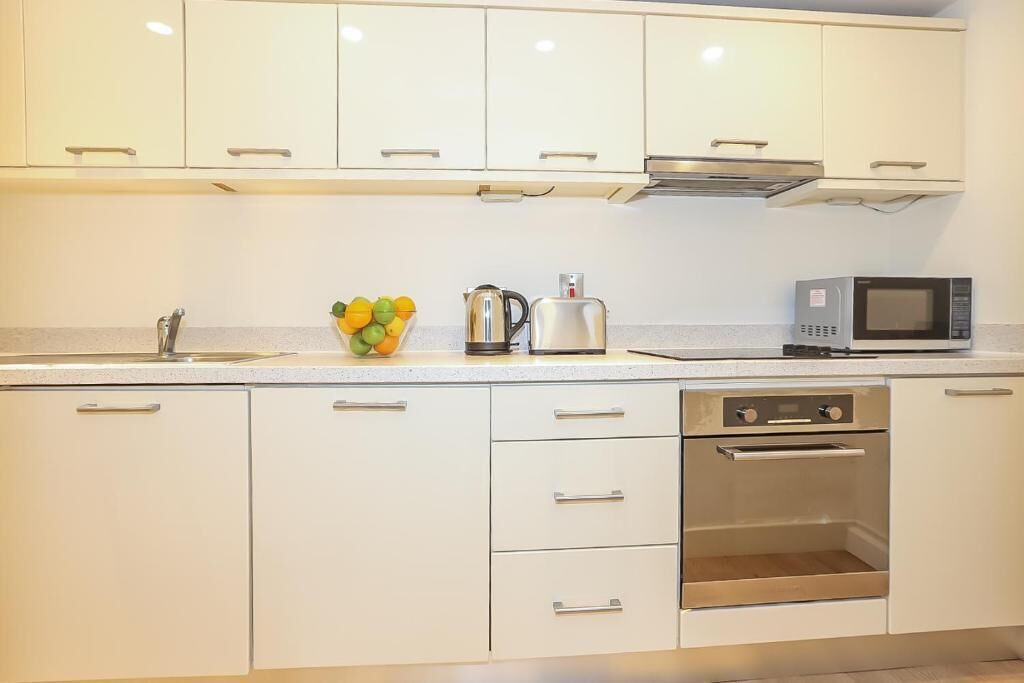 A modern kitchen with white cabinets, a stainless steel oven, a microwave, and a kettle on the countertop.