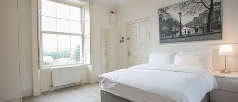 A bedroom with a large window, a bed, a nightstand, and a wall-mounted lamp.