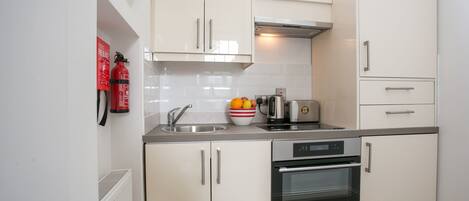 A modern kitchen with white cabinets, a stainless steel sink, a kettle, and a toaster.