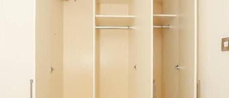 A walk-in closet with open doors, featuring multiple shelves and a central drawer.