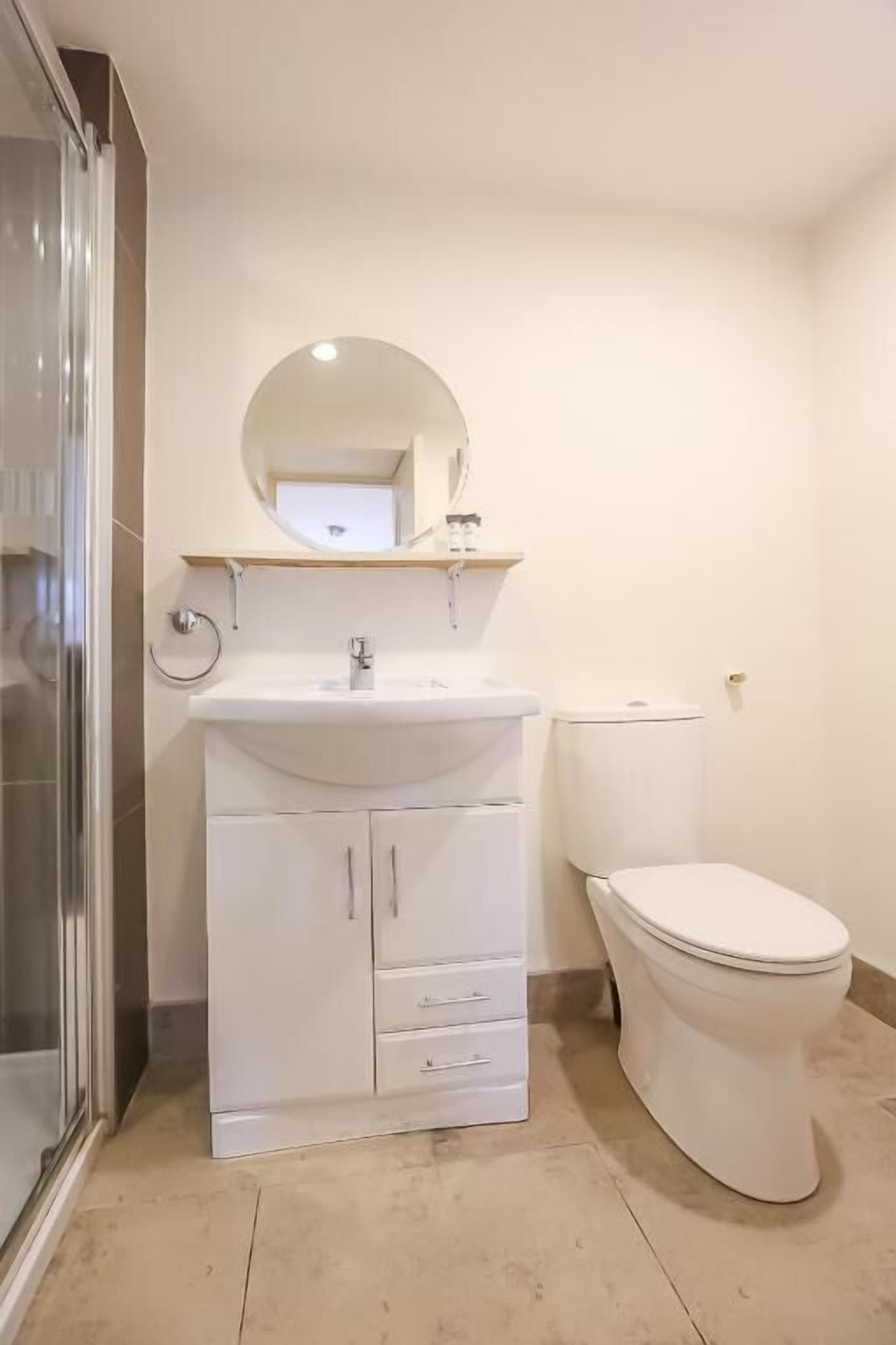 Casa de banho com lavatório branco, espelho e sanita.