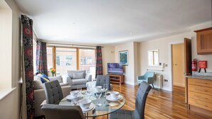 A modern living room with a dining area, large windows, and a flat-screen TV. - Georgian Square Apartments (Dublin)