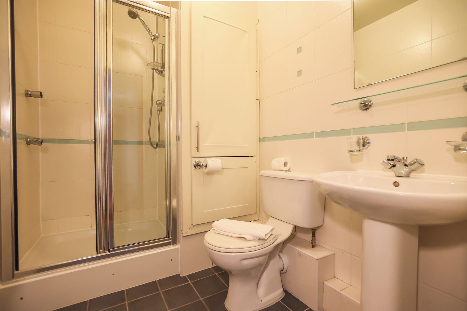 Een badkamer met een douchecabine van glas, een toilet en een wastafel met spiegel.