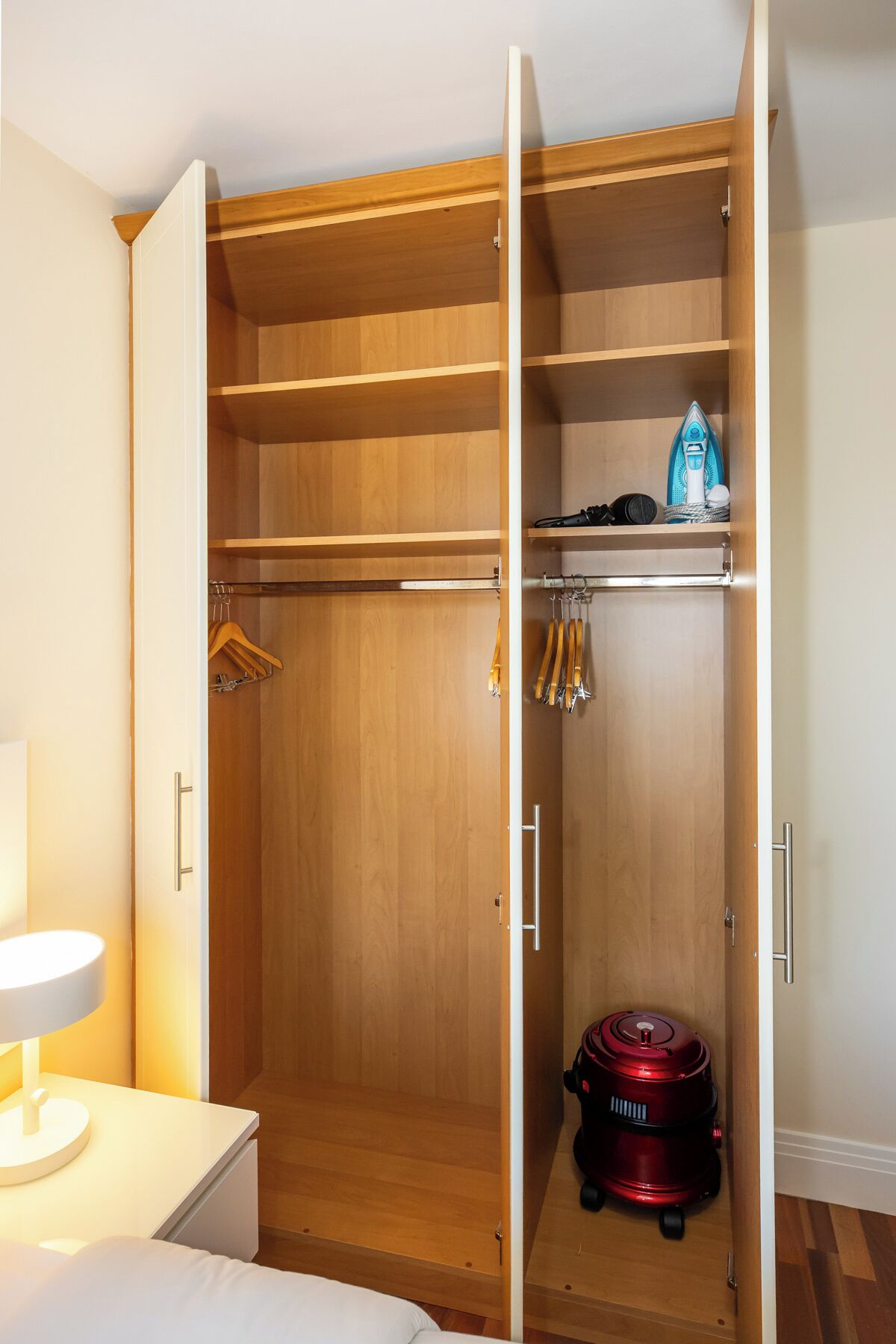 Un vestidor con estantes de madera, una barra para colgar ropa y un aspirador.