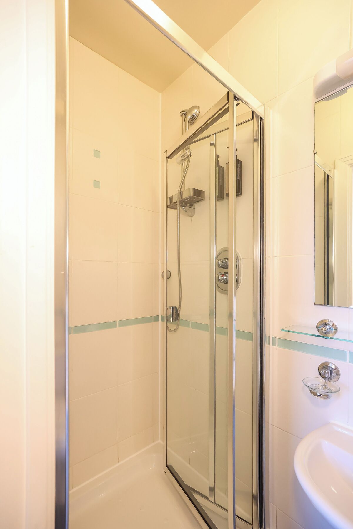 A glass-enclosed shower with a handheld showerhead and a wall-mounted faucet.