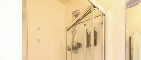 A glass-enclosed shower with a handheld showerhead and a wall-mounted faucet.
