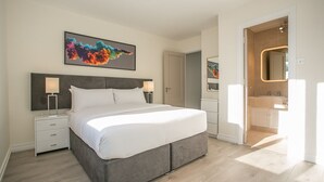 A modern bedroom with a large bed, bedside tables, and a bathroom visible through an open door. - Georgian Square Apartments (Dublin)