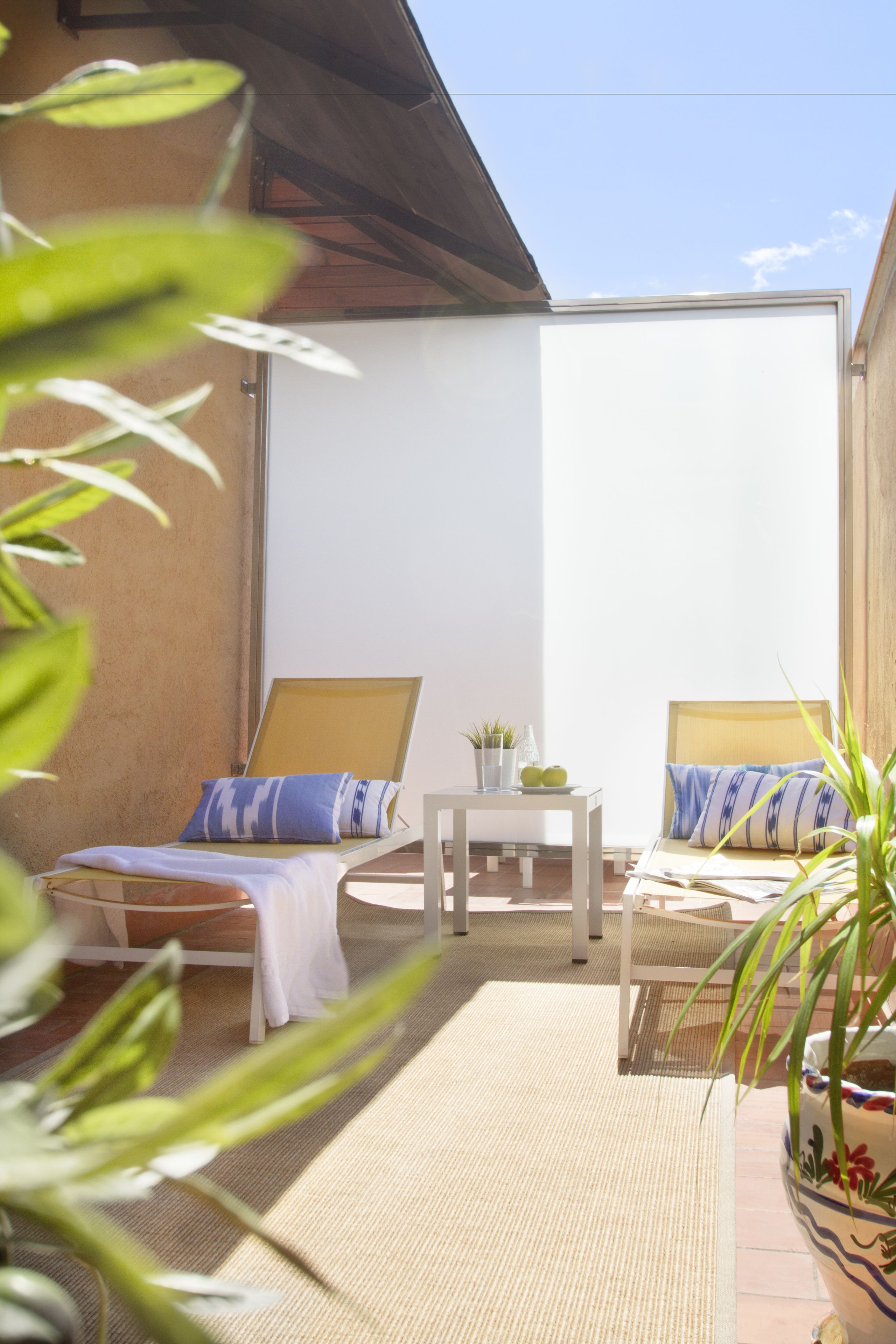 A sunlit patio with two lounge chairs, a small table, and a potted plant.