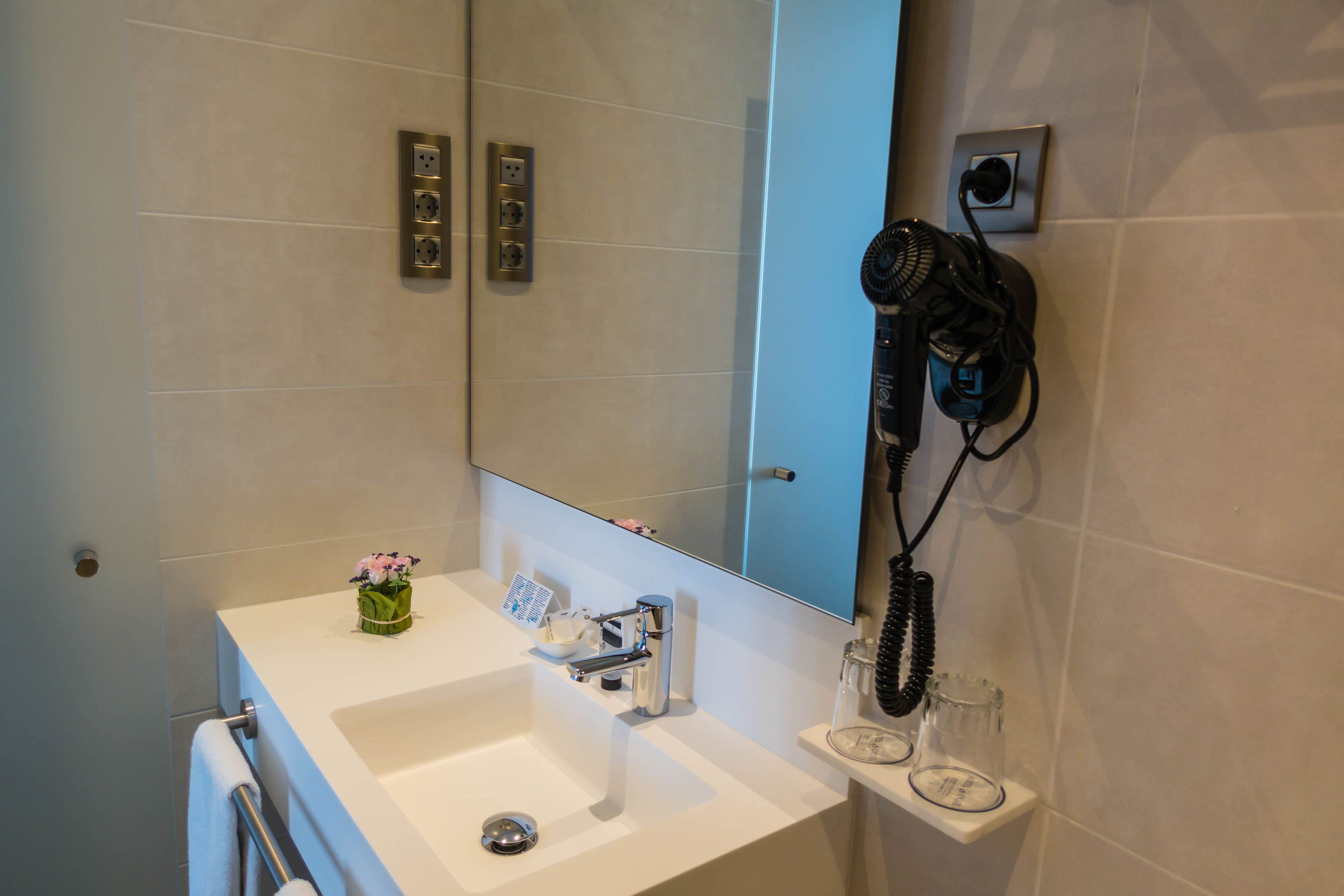 Ein Badezimmer mit einem weißen Waschbecken, einem Spiegel und einem an der Wand befestigten Föhn.