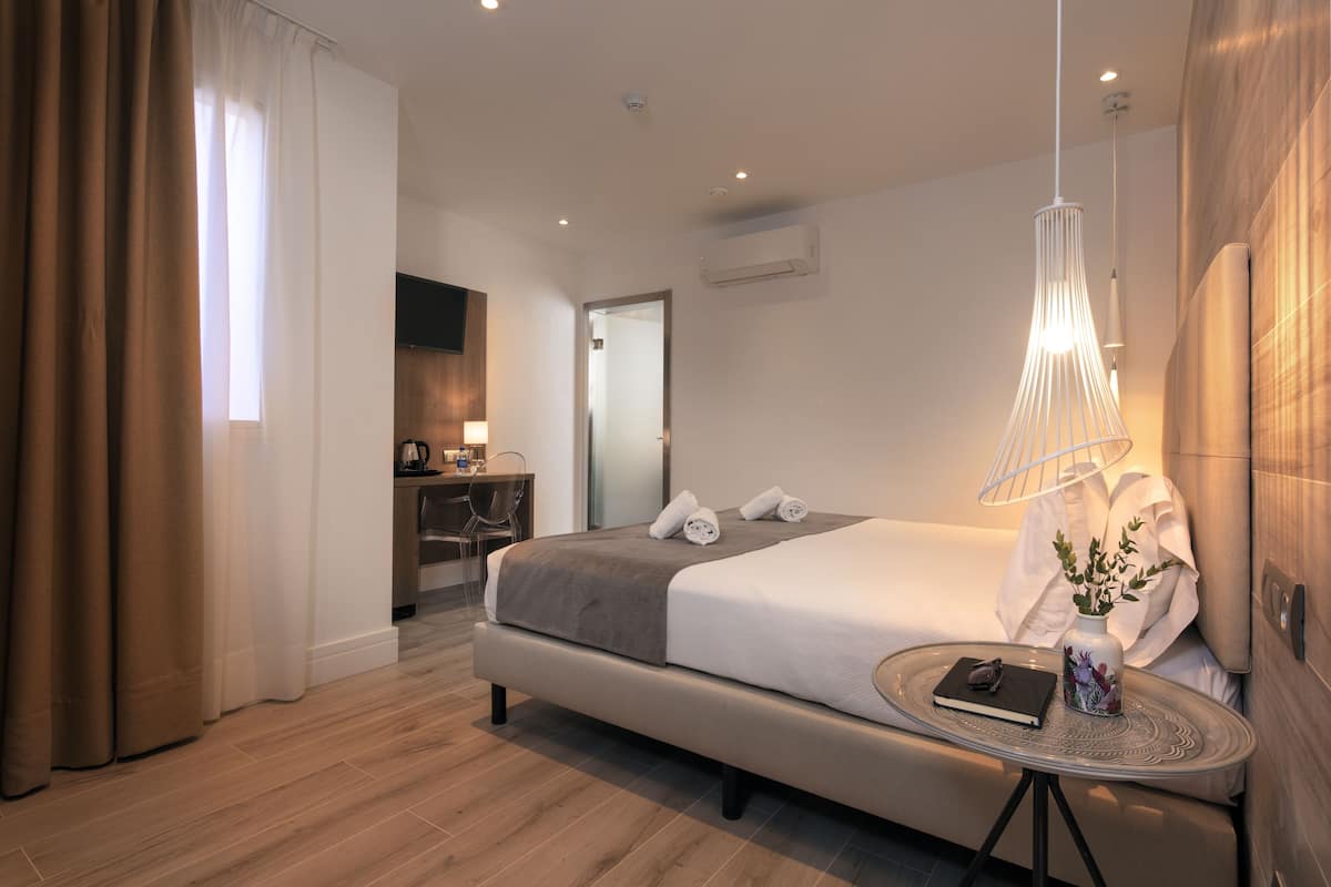 Moderni hotellihuone, jossa on suuri sänky, pyöreä pöytä maljakolla ja työpöytä tuolilla.