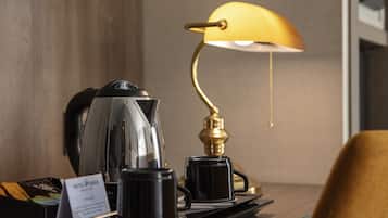 A hotel room with a coffee station, including a coffee pot, cups, and a sign.