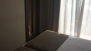 Een hotelkamer met een bed, een flatscreen-tv aan de muur en een raam met dunne gordijnen.