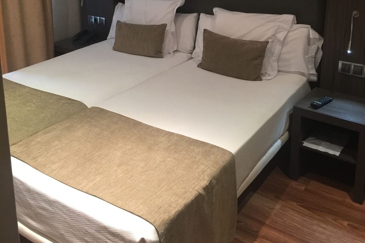 Hotellihuone, jossa on suuri sänky, kaksi tyynyä, yöpöytä ja pieni sivupöytä.