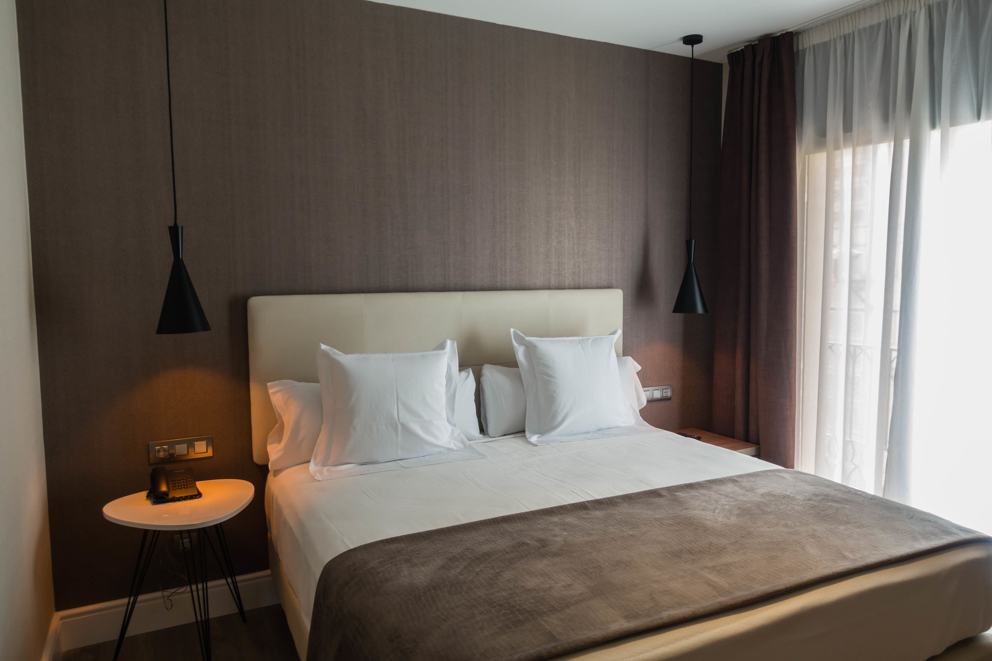 Una habitación de hotel con una cama grande, una mesita de noche, una lámpara y una ventana con cortinas.