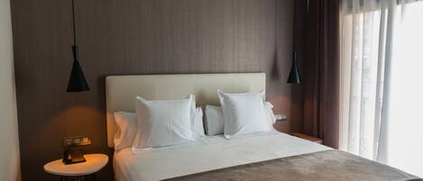 Ein Hotelzimmer mit einem großen Bett, einem Nachttisch, einer Lampe und einem Fenster mit Vorhängen.