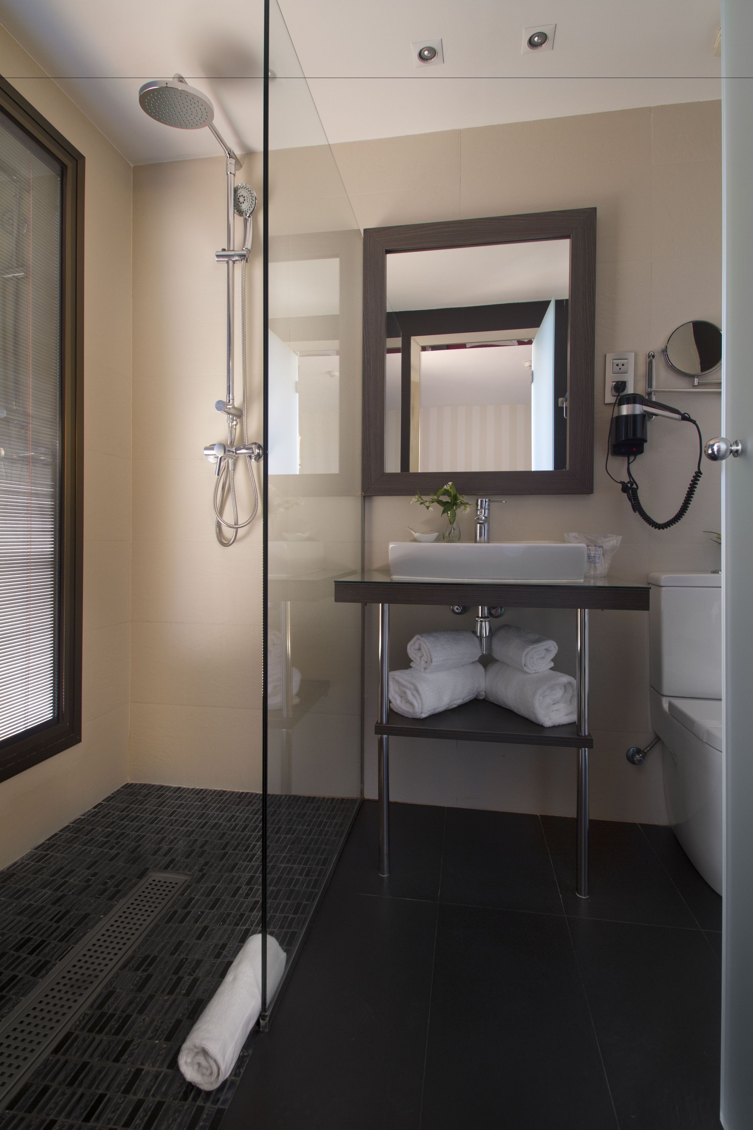 Un baño moderno con cabina de ducha de vidrio, un lavamanos, un espejo y un perchero para toallas.