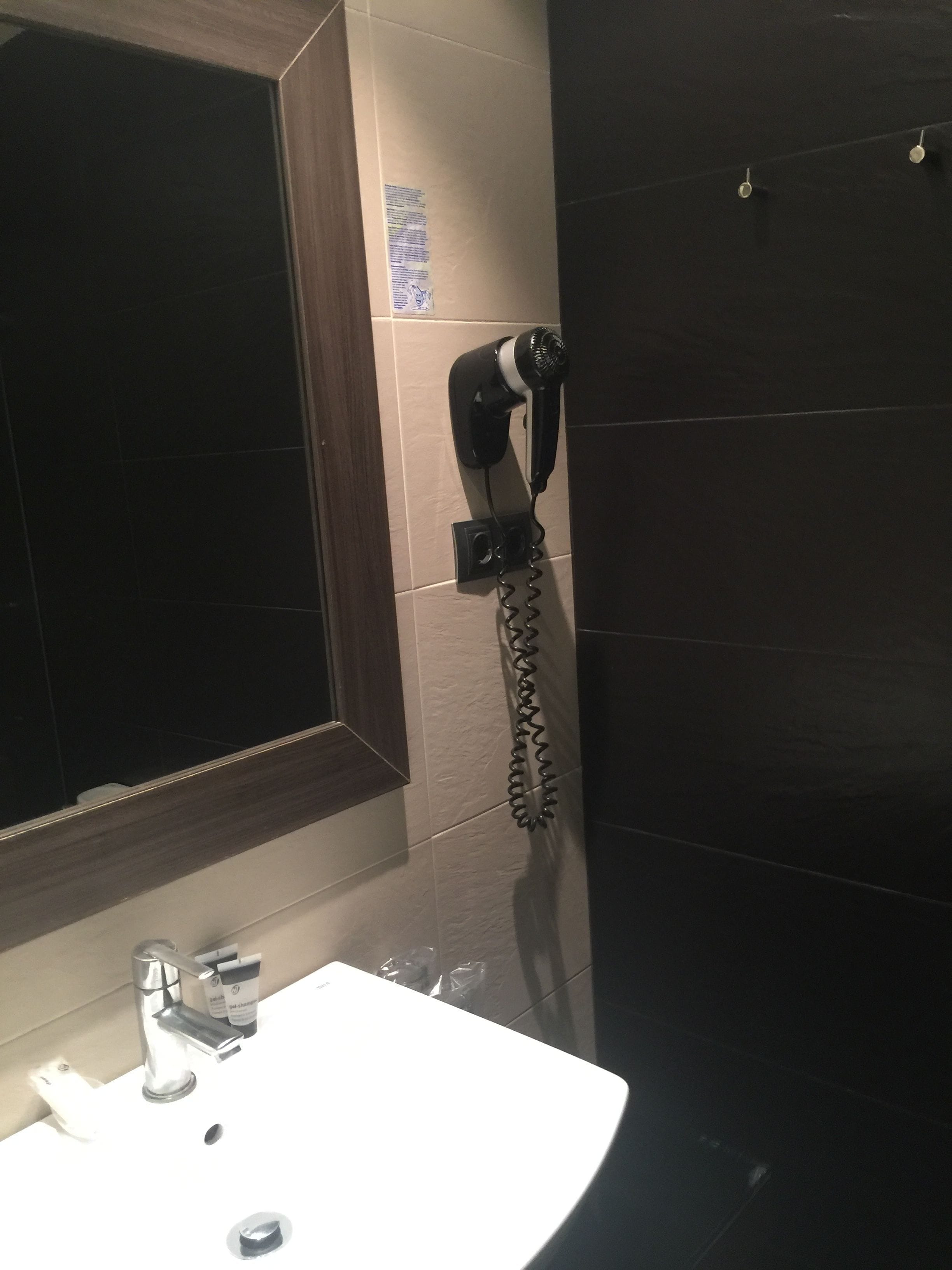 Une salle de bain équipée d’un lavabo, d’un sèche-cheveux fixé au mur et d’un miroir.