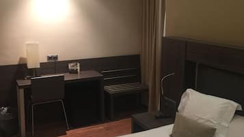 Hotelkamer met een bed, bureau, stoel, lamp en raam met gordijnen.