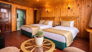 Een kamer met houten vloer, twee bedden, een kamerplant cactus en een ronde tafel.