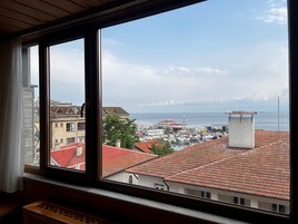 Vista desde una ventana que da a un puerto deportivo con barcos, cielo despejado y edificios con tejados de tejas rojas.