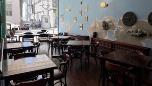 A restaurant interior with wooden tables and chairs, a blue wall with decorative elements, and a view of the street outside. - Denizci Hotel (Sinop)
