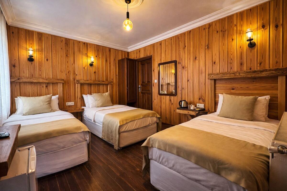A room with wooden panel walls, three beds, a wooden headboard, a mirror, and a hanging light fixture.