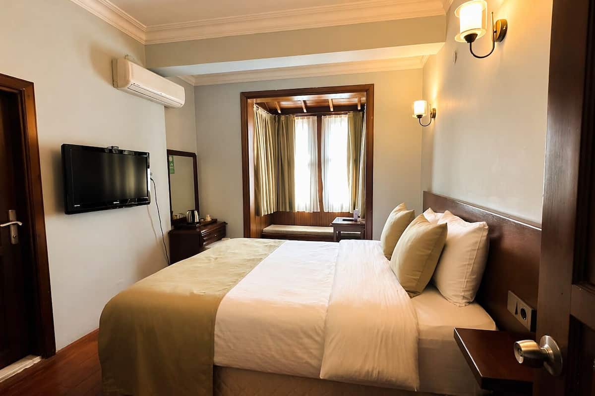 A hotel room with a bed, a television, a desk, and a window with curtains.