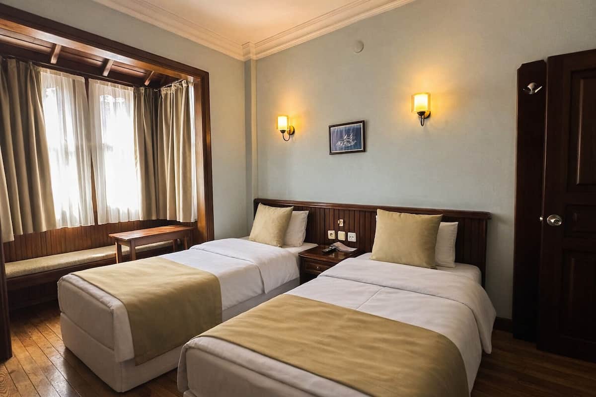 A hotel room with two beds, a bench, a nightstand, and a window with curtains.