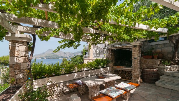 An outdoor seating area with stone benches and a pergola, overlooking a scenic view of the sea and mountains. - Villa Larsen (Omis)