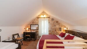 A cozy attic bedroom with a stone wall, a wooden bed, a desk, and a chair. - Villa Larsen (Omis)