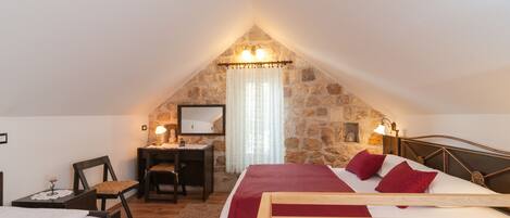 A cozy attic bedroom with a stone wall, a wooden bed, a desk, and a chair.