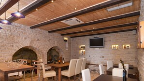 A rustic interior with stone walls, wooden beams, and a stone fireplace. Tables and chairs are arranged for dining. - Villa Larsen (Omis)