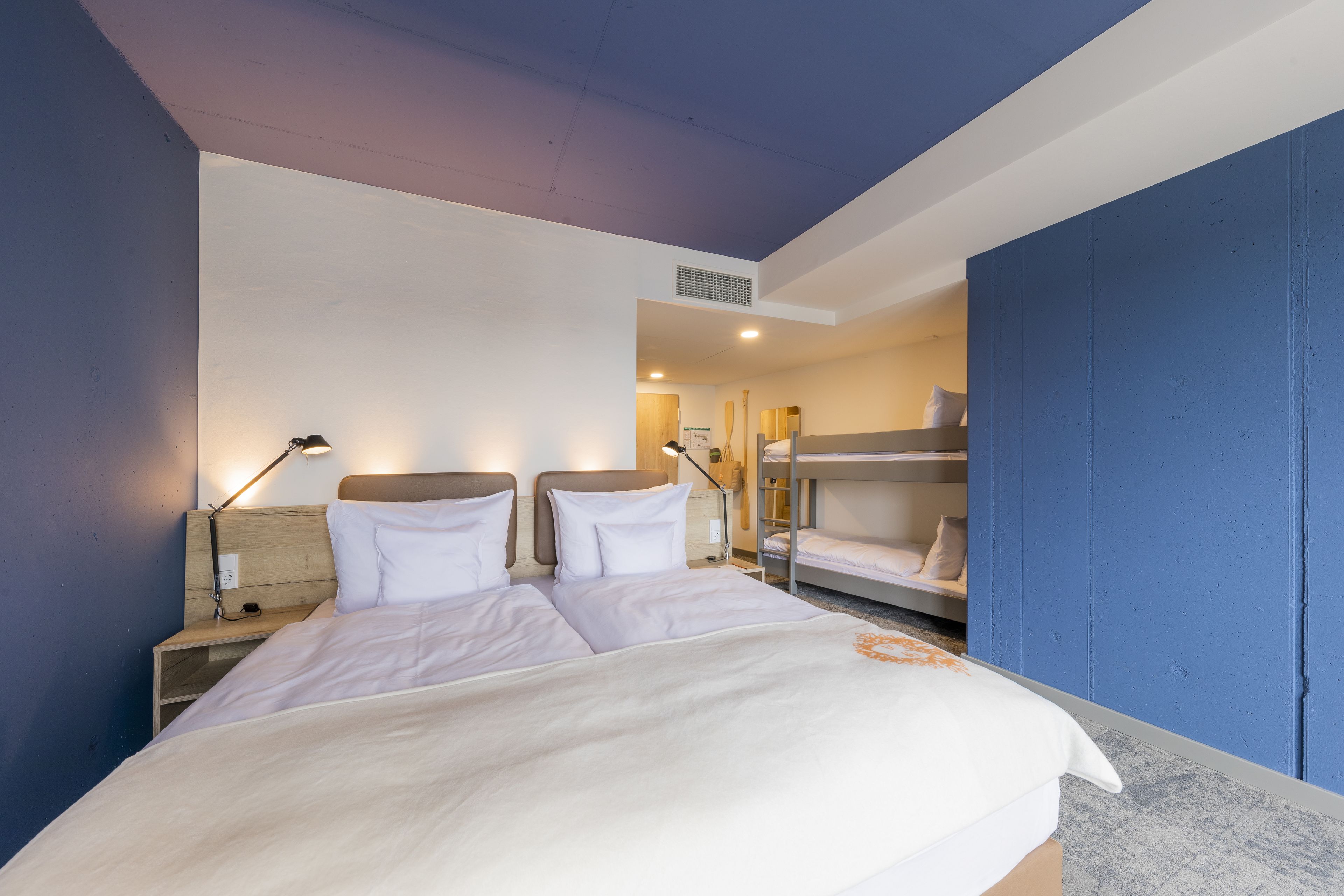 Una habitación de hotel con una cama grande, una mesita de noche, un escritorio y una cama litera.