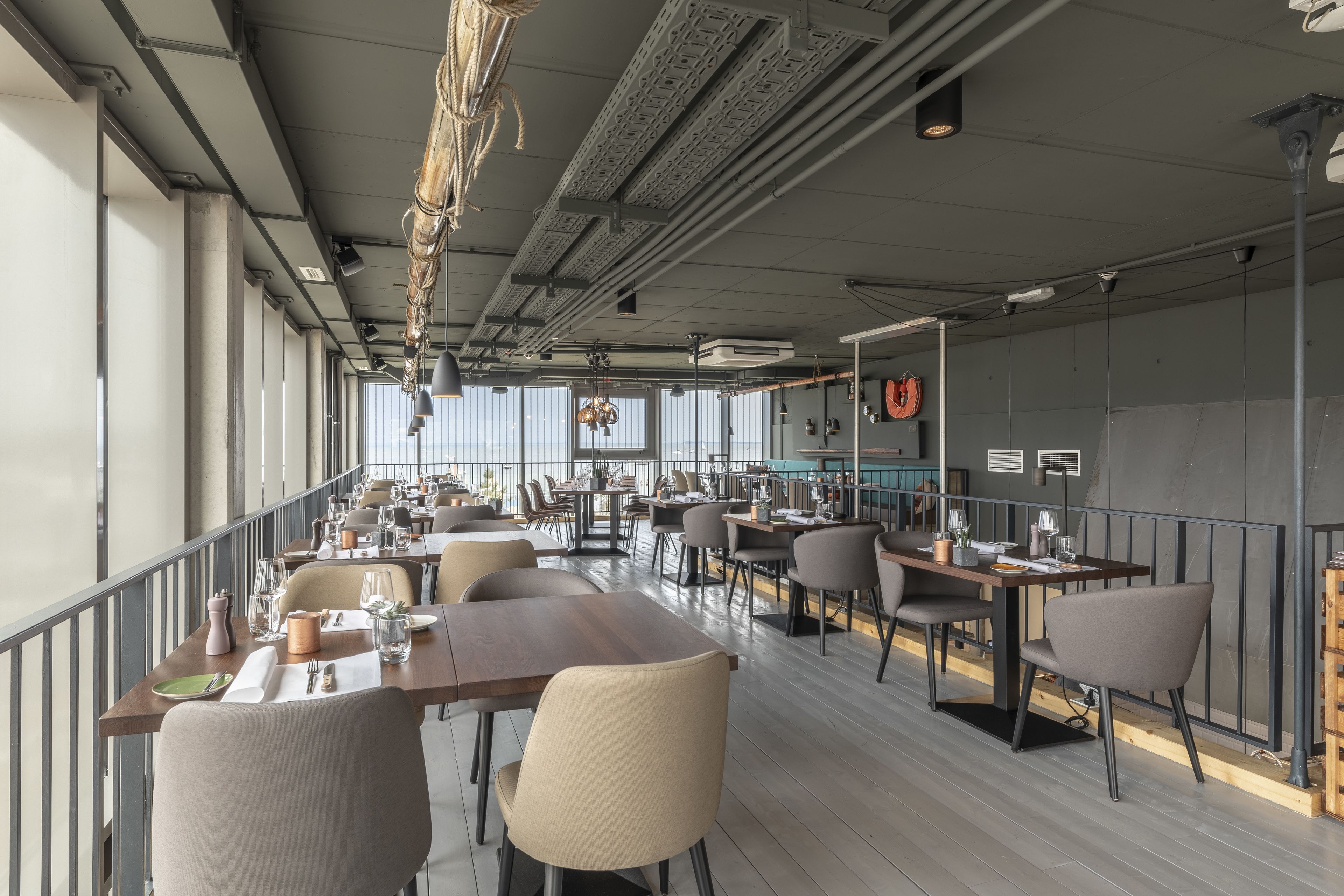 A modern restaurant with long communal tables, high ceilings, and large windows.