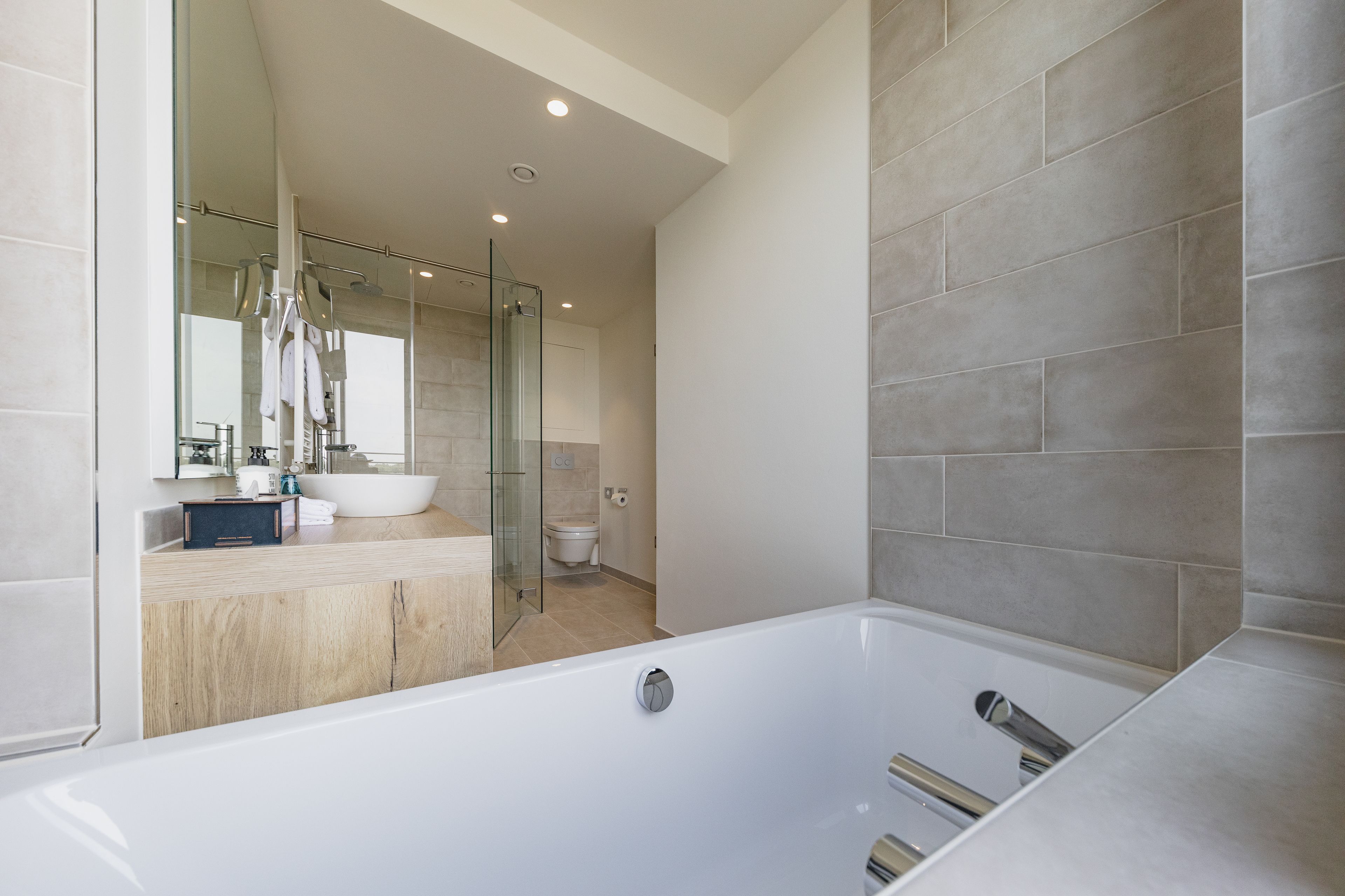 A modern bathroom with a large bathtub, a glass shower enclosure, and a wooden vanity.