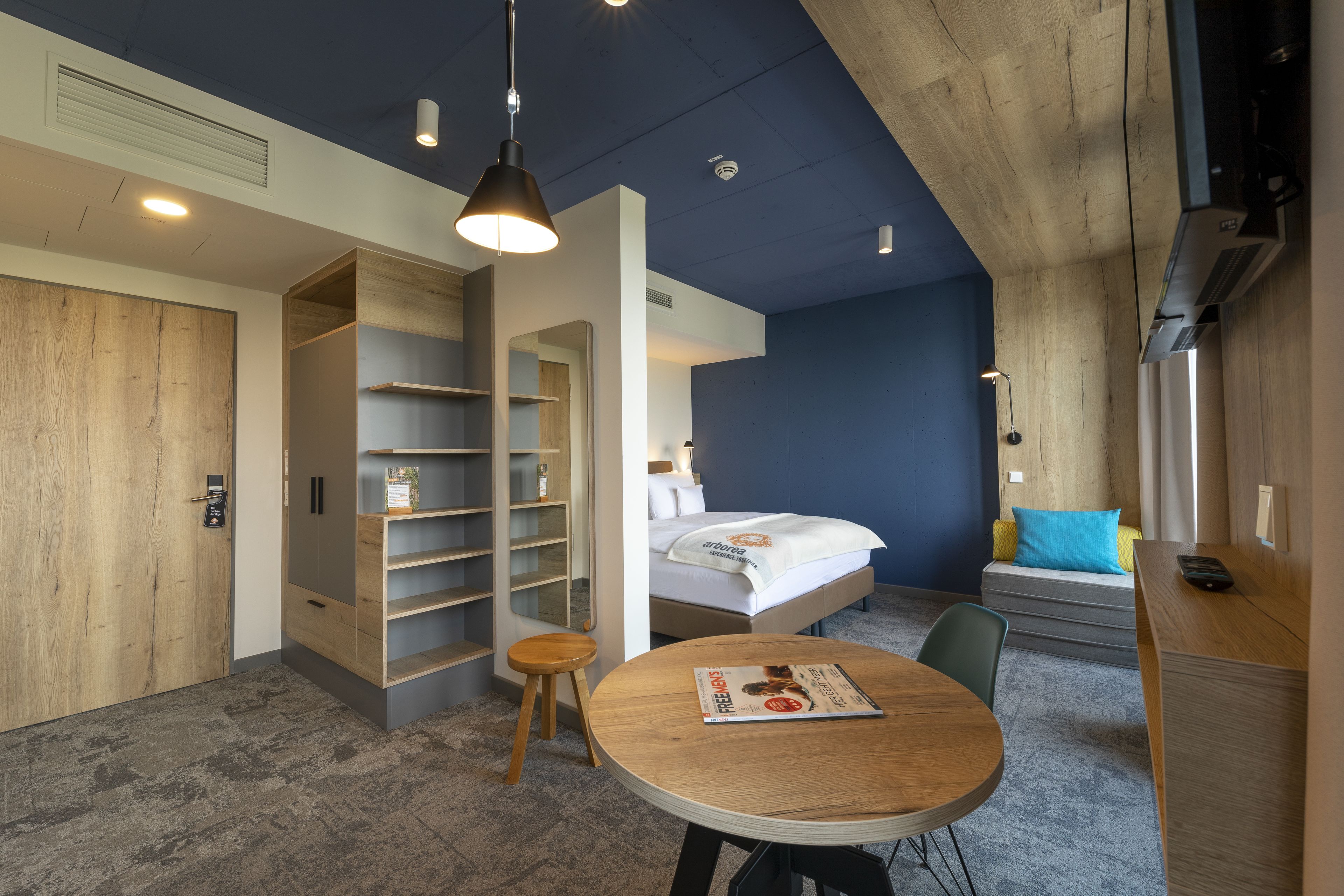 Una habitación de hotel moderna con una cama, un escritorio, una mesa redonda y estanterías empotradas.