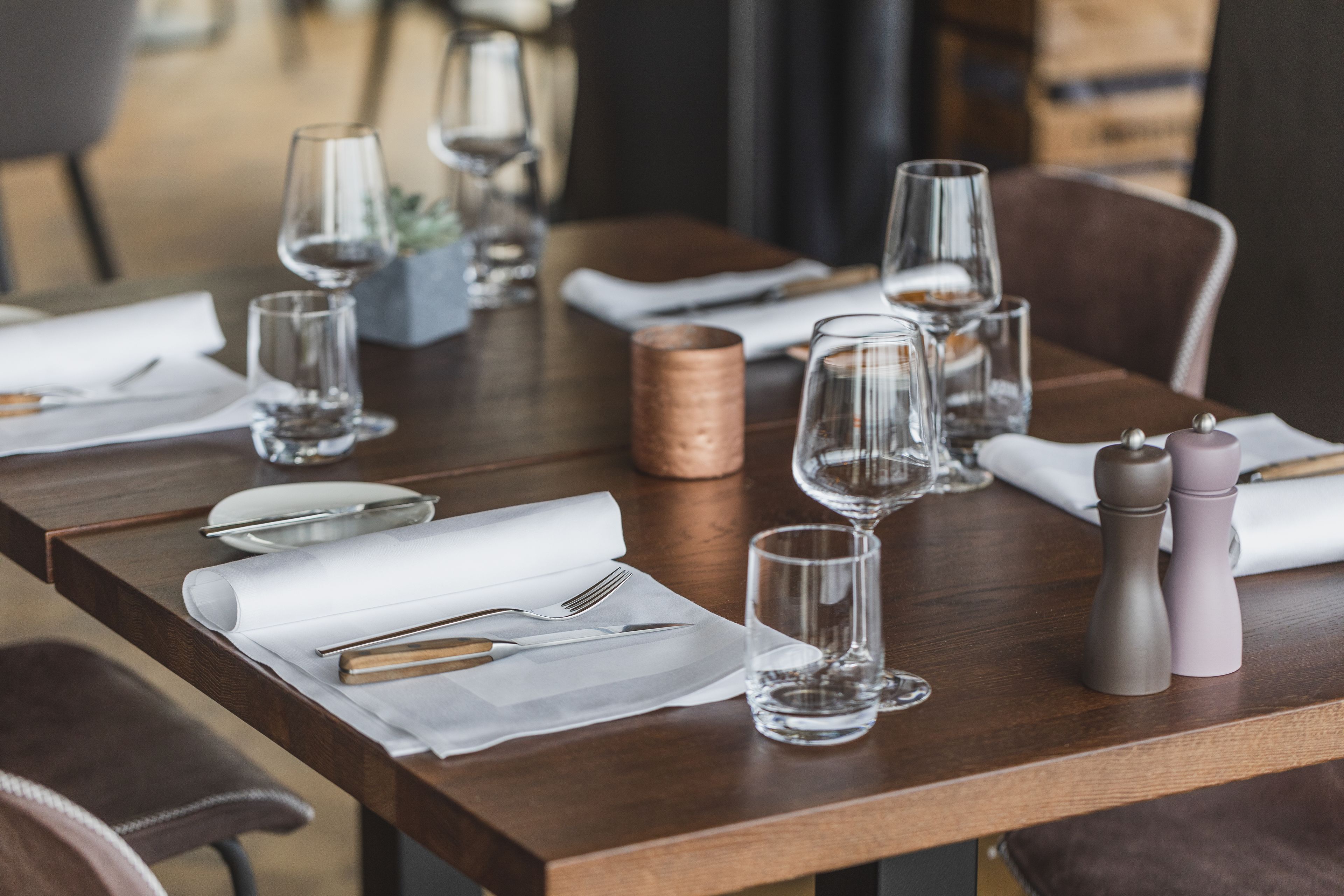A neatly set dining table with clear glassware, cutlery, and napkins.